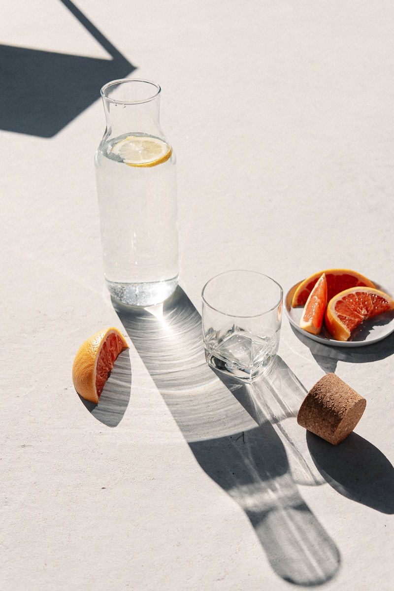 clear drinking glass beside sliced orange fruit on white table